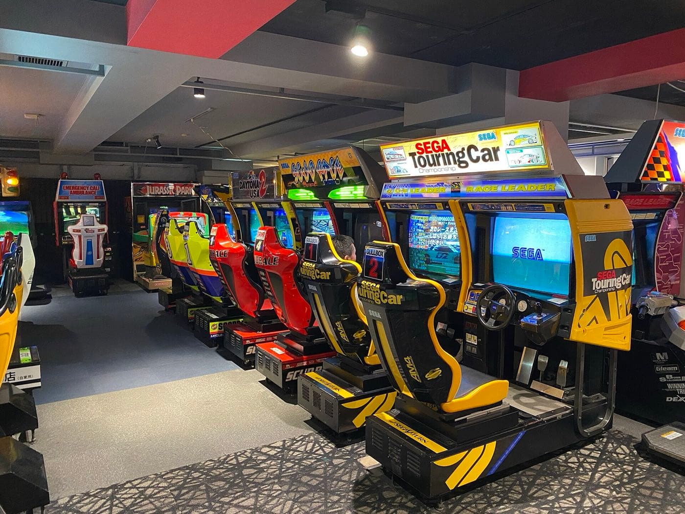 Row of driving arcade cabinets with racing seats in a retro games floor