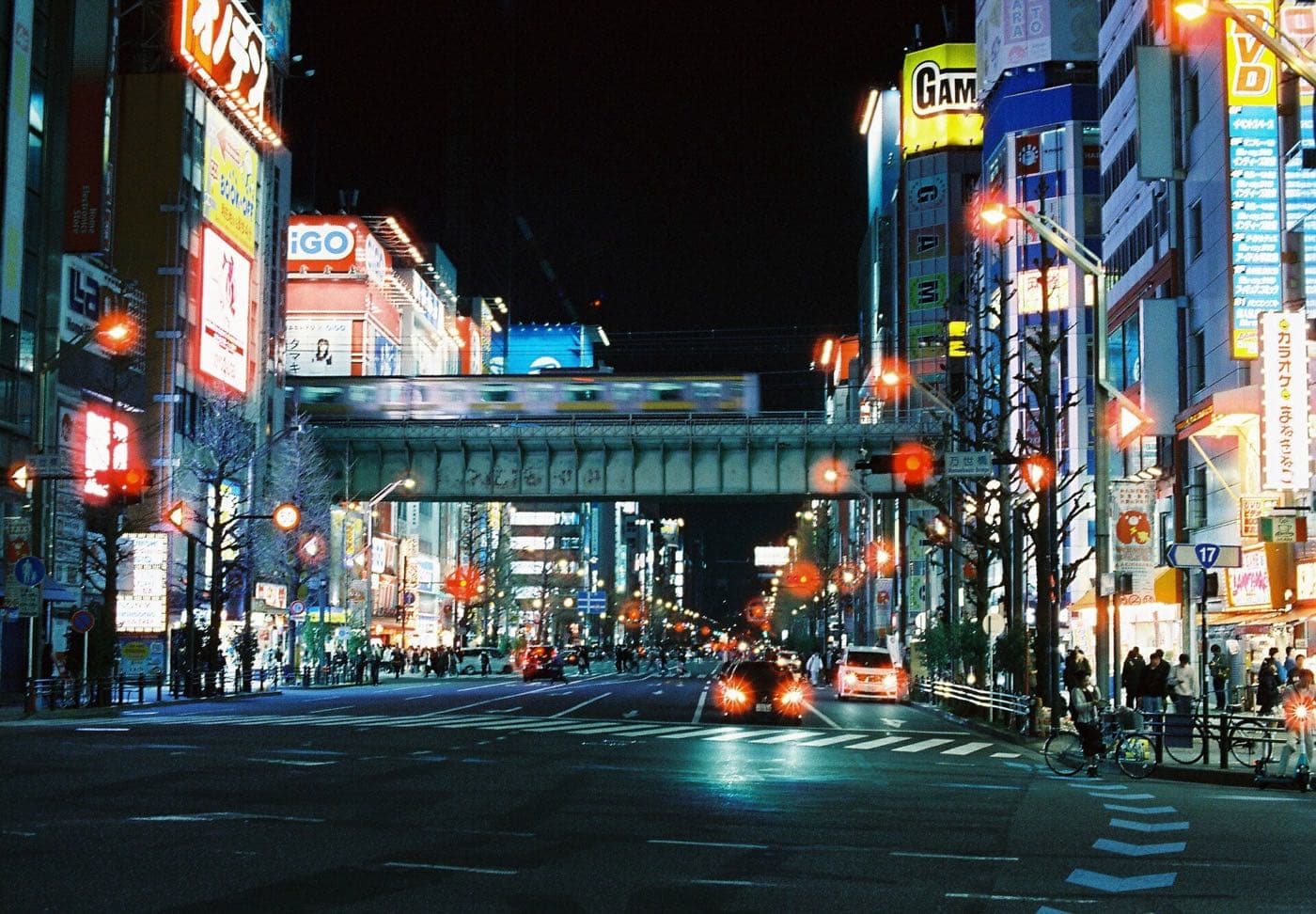 Akihabara's main street at night with illuminated signs and a railway overpass in the distance