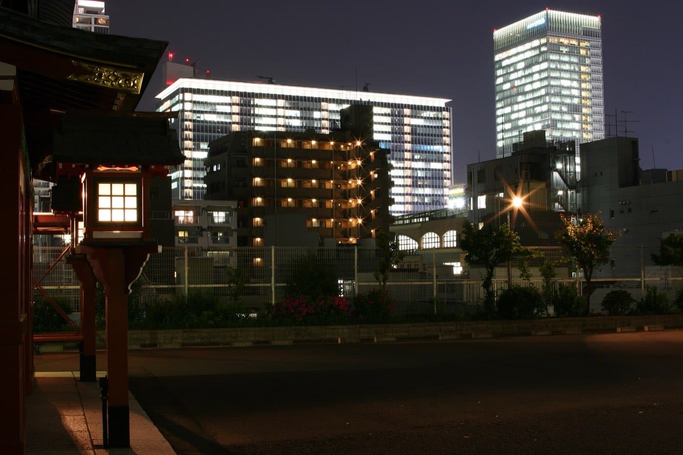 Night view of lit office buildings seen past a shrine lantern
