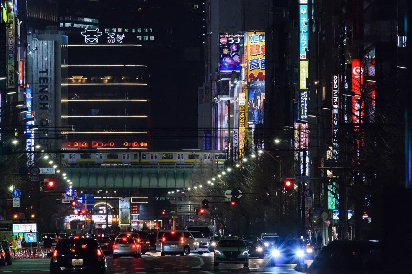Night traffic on Akihabara's main street with neon signs and a train crossing the overpass