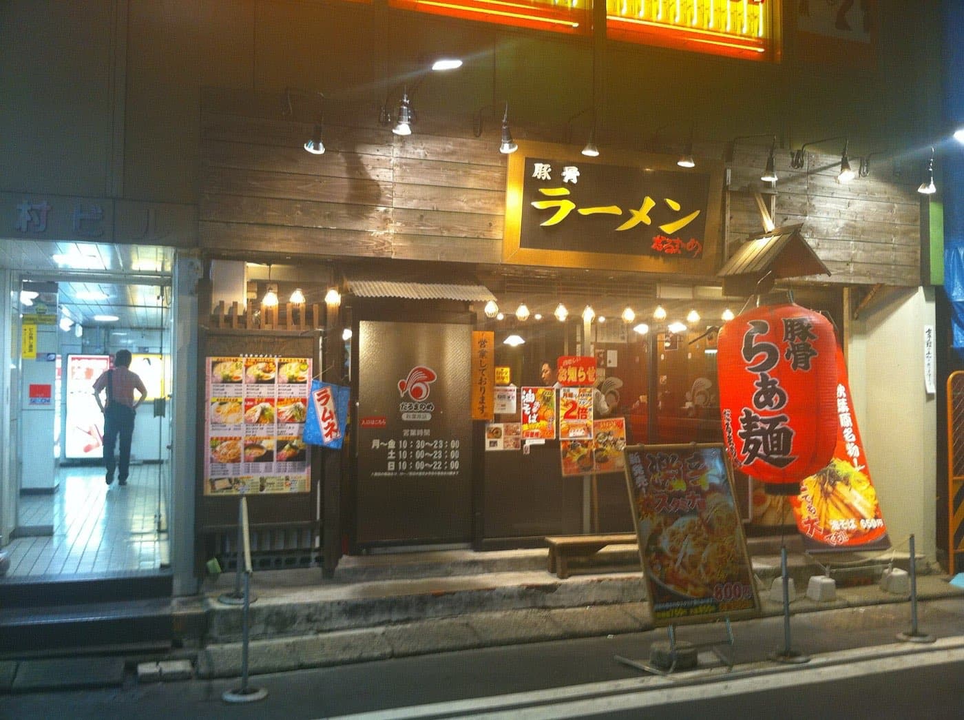 Front of a ramen shop at night with a red paper lantern and menu boards